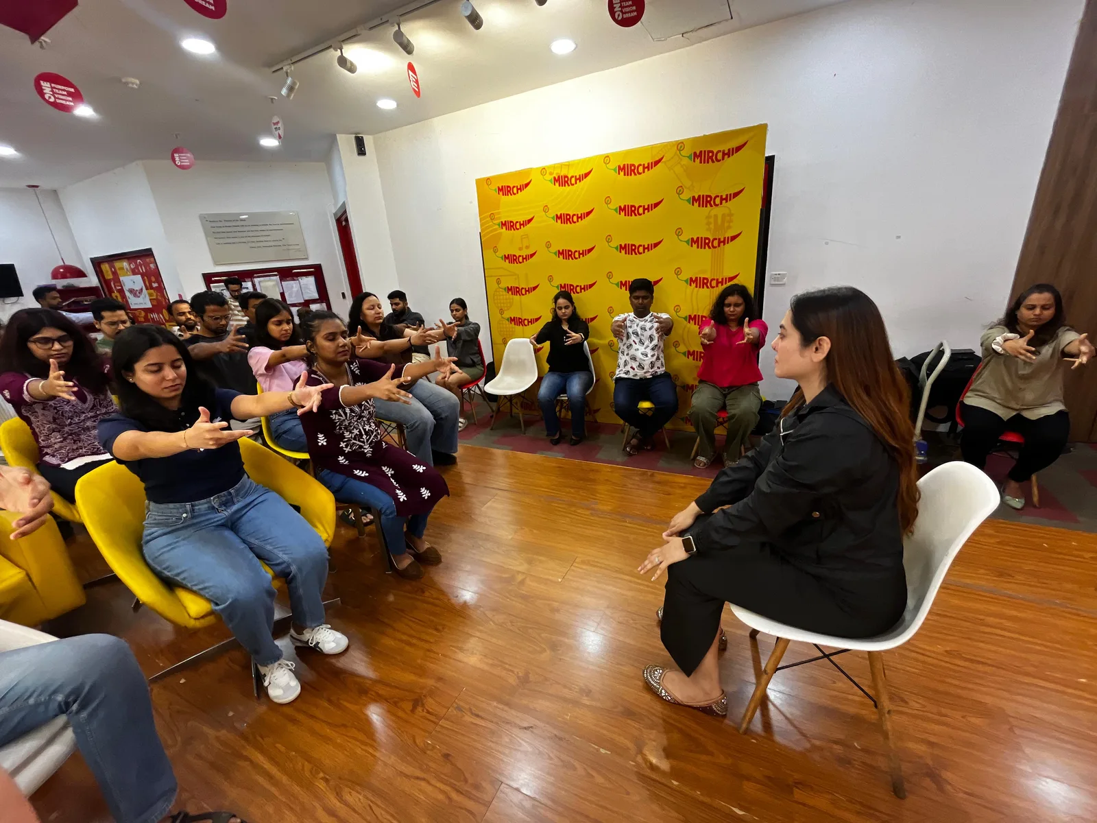 Vibha Jain seated in front of a group of participants who are following a guided focus and relaxation exercise with their arms extended and eyes closed.