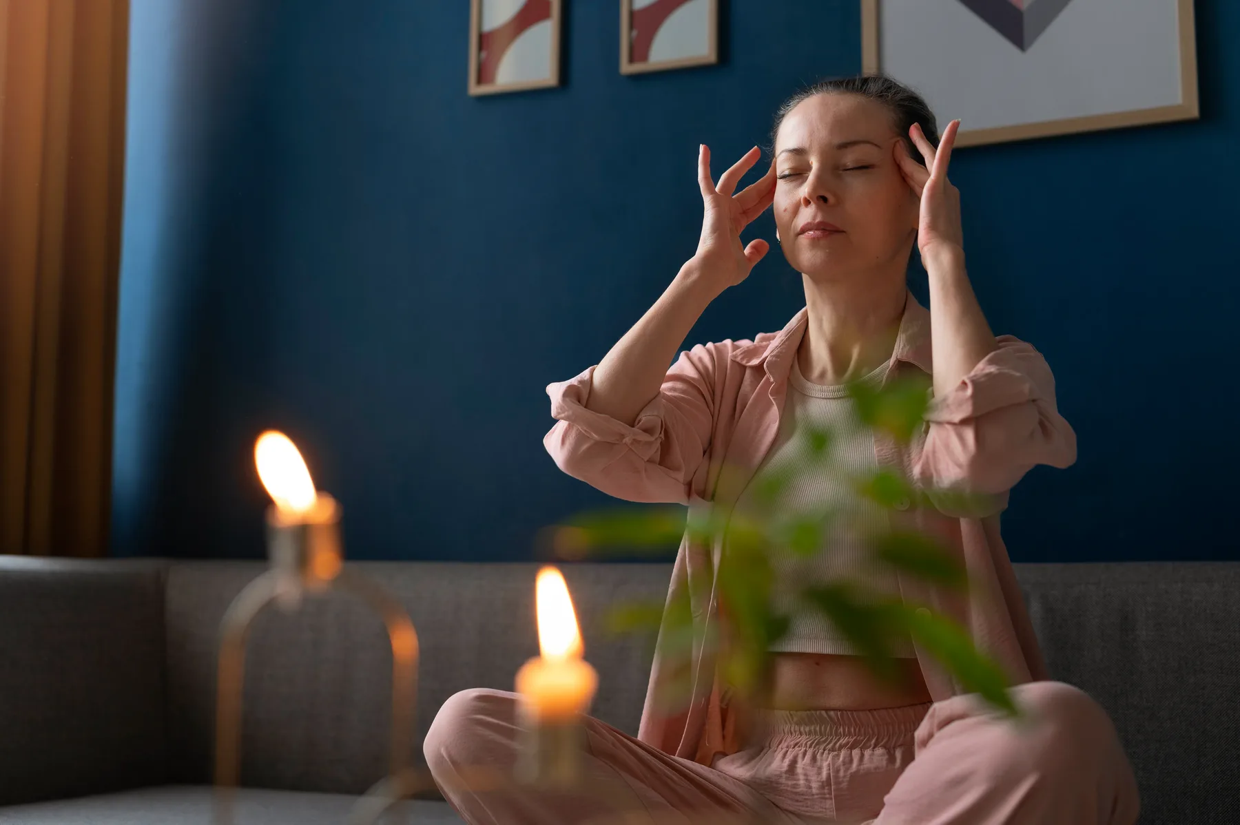 A woman sitting calmly with her eyes closed and fingertips at her temples, taking a quiet moment of focused relaxation at home.
