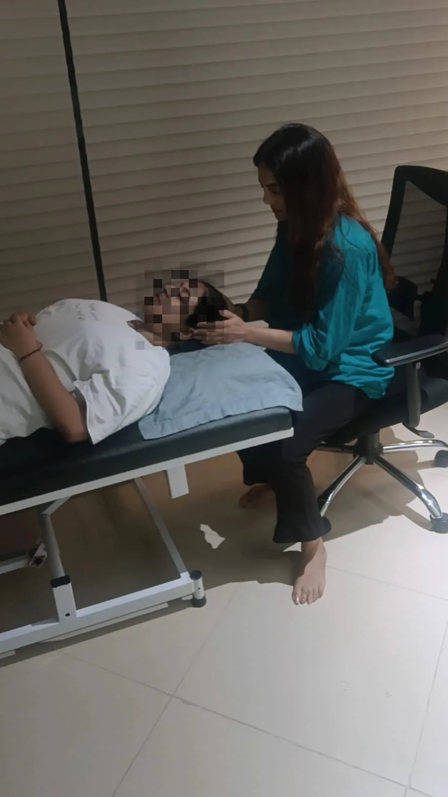 Vibha Jain seated beside a reclined client during a guided hypnotherapy session. The client's face has been obscured to protect their privacy.